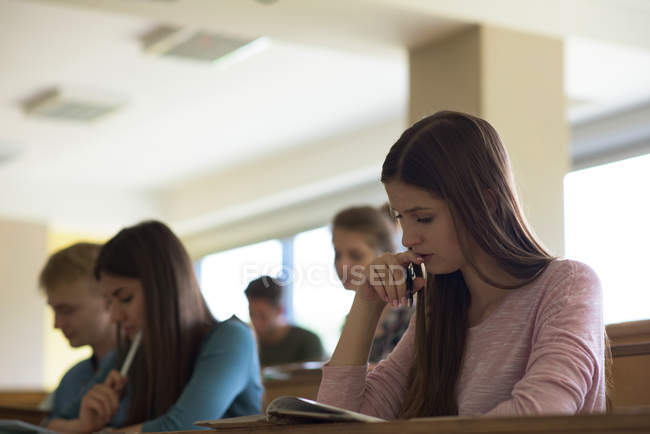 Vista a basso angolo dei giovani studenti universitari alla scrivania mentre sono seduti in classe — Foto stock