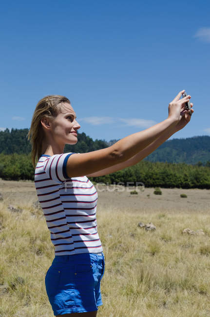 Vista lateral de uma mulher caminhante sorrindo tomando selfie enquanto está em campo — Fotografia de Stock