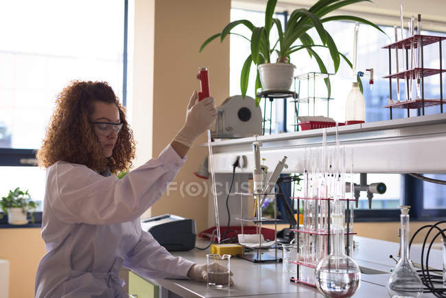 Adolescente tenant une pipette tout en pratiquant l'expérience de chimie au bureau en laboratoire — Photo de stock