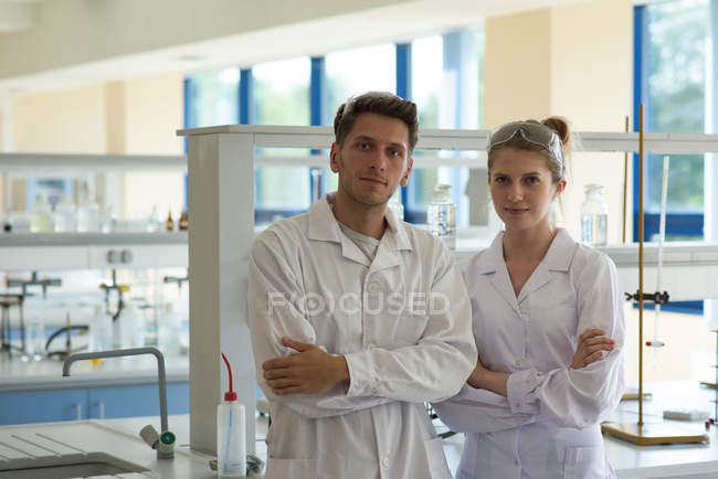 Retrato de estudiantes universitarios con los brazos cruzados de pie en el laboratorio - foto de stock
