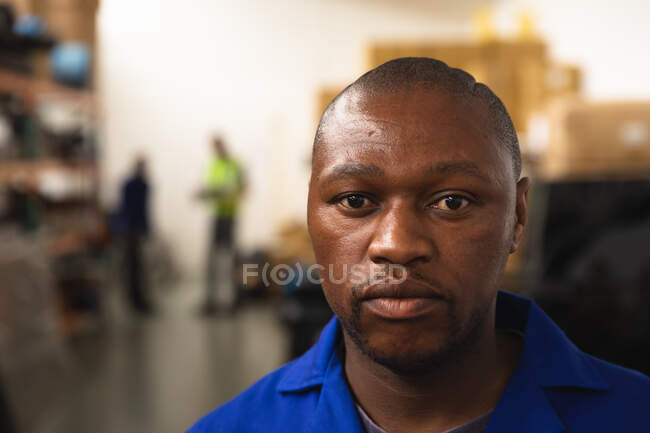 Portrait of an African American male worker wearing a workwear, in a storage warehouse at a factory making wheelchairs, looking at camera — Stock Photo