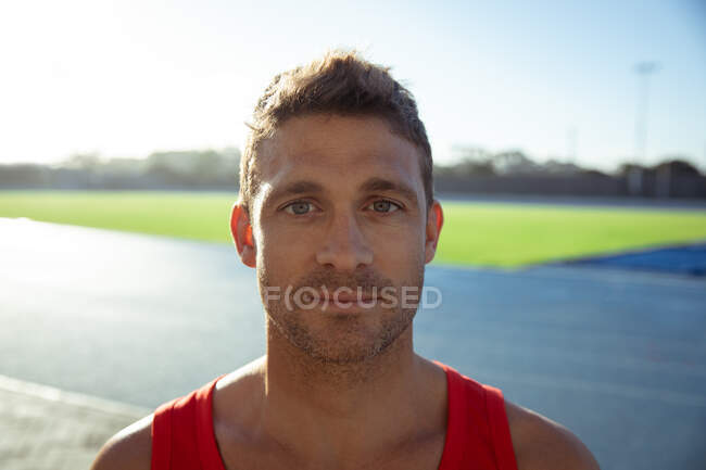 Porträt eines selbstbewussten kaukasischen Athleten, der in einem Sportstadion übt und dabei eine rote Weste trägt und direkt in die Kamera blickt — Stockfoto