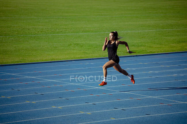 Vue latérale d'une athlète blanche pratiquant dans un stade de sport, sprint. — Photo de stock