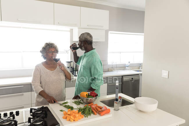 Un couple afro-américain sénior passe du temps à la maison ensemble, distance sociale et isolement personnel en quarantaine pendant l'épidémie de coronavirus covid 19, tenant des verres de vin rouge et buvant — Photo de stock