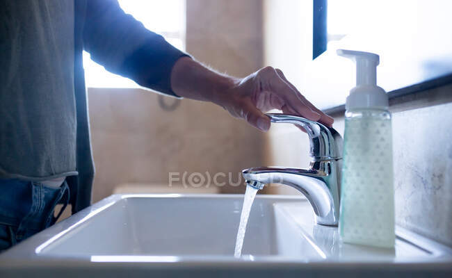 Mid section of woman at home in bathroom during daytime running water from tap before washing her hands in a basin — Stock Photo