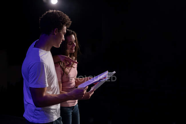 Side view of Caucasian teenage boy and girl holding scripts and performing on the stage of a school theatre during rehearsals for a performance — Stock Photo