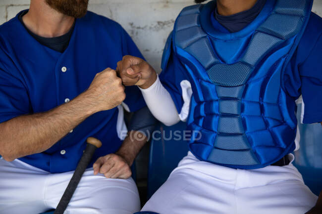 Front view mid section of two baseball players, preparing before a game, sitting in a changing room, fist bumping — Stock Photo