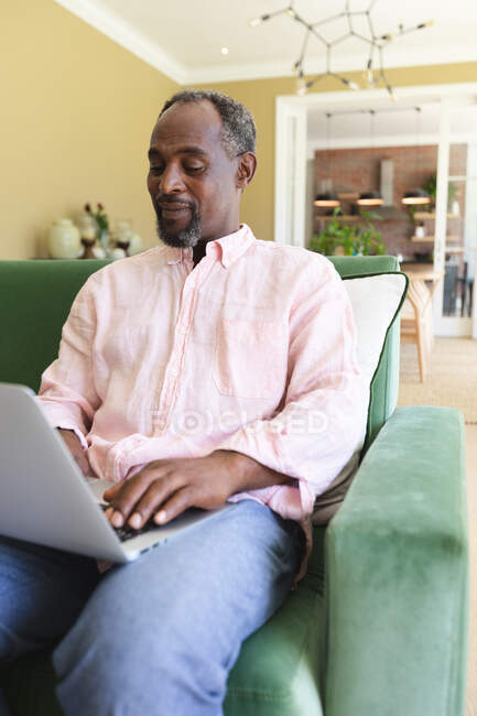 Close up of a happy handsome senior retired African American man at home sitting in an armchair in his living room, using a laptop computer and smiling, self isolating during coronavirus covid19 pandemic — Stock Photo