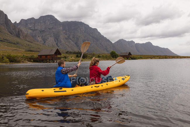Vista lateral de una pareja caucásica pasando un buen rato en un viaje a las montañas, kayak en un lago - foto de stock