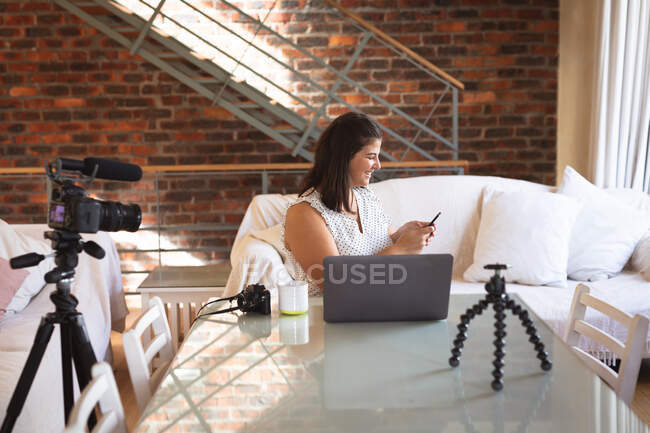 Kaukasische Vloggerin zu Hause, in ihrem Wohnzimmer mit Kamera und Smartphone, während sie ihren Online-Blog vorbereitet. Soziale Distanzierung und Selbstisolierung in Quarantäne. — Stockfoto