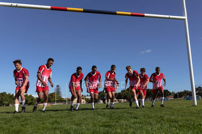 Вид спереди подростковой многонациональной мужской команды игроков в регби в командном раздевании, разогревающейся на игровом поле. — стоковое фото