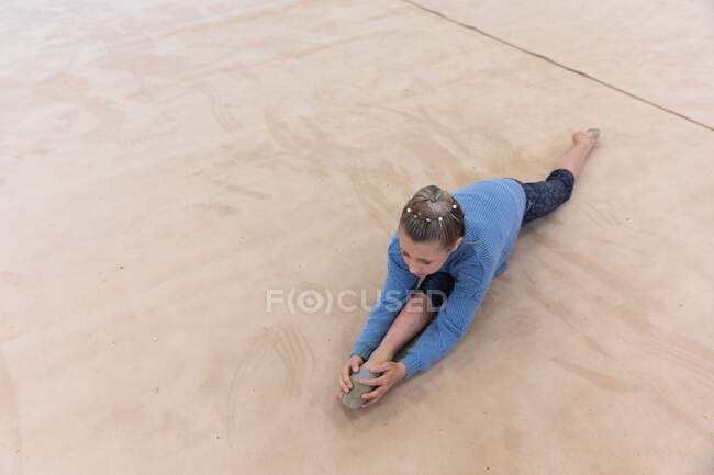 Vista laterale ad alto angolo della ginnasta femminile caucasica adolescente che si esercita in palestra, si divide, si estende e si riscalda. — Foto stock