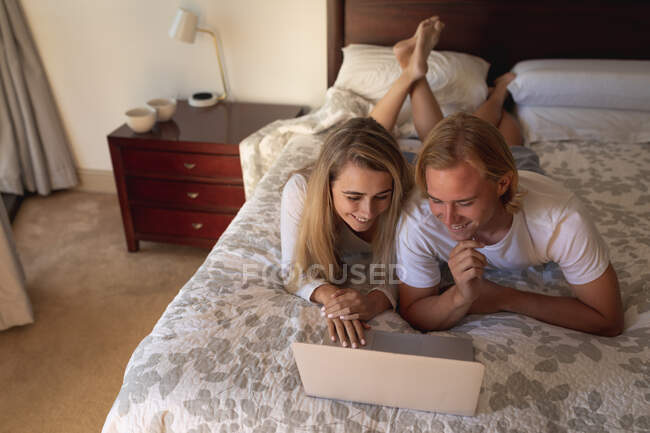 Casal caucasiano deitado na cama juntos, usando um laptop. Distanciamento social e auto-isolamento em quarentena. — Fotografia de Stock