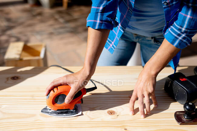 Mid section of woman spending time at home self isolating and social distancing in quarantine lockdown during coronavirus covid 19 epidemic, doing DIY in her garden, sanding wood. — Stock Photo