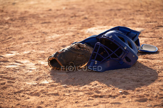 Close up detail of a baseball equipment, helmet, glove and a pad lying on a baseball field on a sunny day — Stock Photo