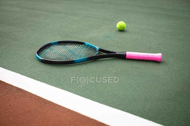 Primer plano de una raqueta de tenis junto a una pelota de tenis en una cancha de tenis en un día soleado - foto de stock