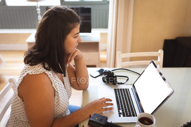 Caucasian female vlogger at home, in her sitting room using a laptop to prepare her online blog. Social distancing and self isolation in quarantine lockdown. — Stock Photo