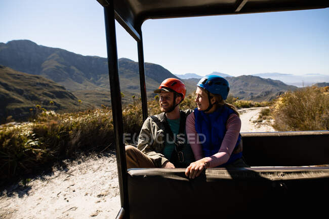Front view of Caucasian couple enjoying time in nature together, in zip lining equipment sitting in a car, embracing on a sunny day in mountains — Stock Photo