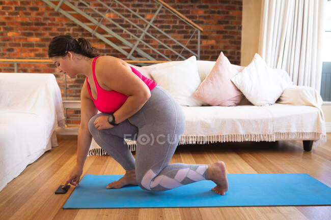 Mulher branca vlogger em casa em sua sala de estar, demonstrando exercícios para seu blog on-line, usando seu smartphone. Distanciamento social e auto-isolamento em quarentena . — Fotografia de Stock