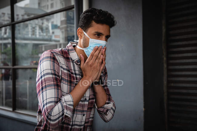 Vista frontal de cerca de un hombre caucásico con camisa a cuadros y máscara facial contra la contaminación del aire y covid19 coronavirus, caminando por la calle y cubriéndose la cara mientras tose. - foto de stock