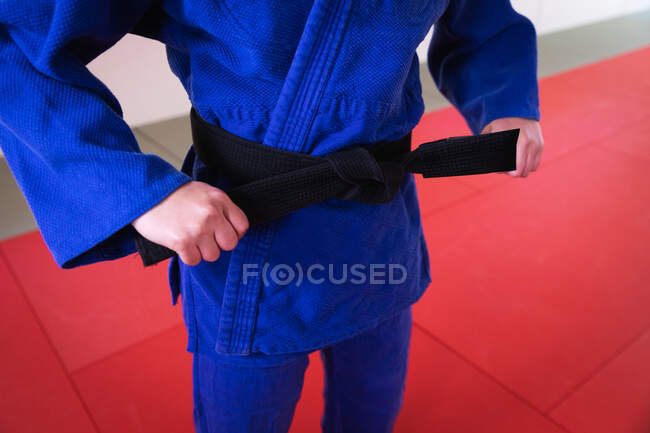 Вид спереду посередині секції джудоки, що стоїть на спортивних килимках, зав'язавши чорний пояс синього джудогі . — стокове фото