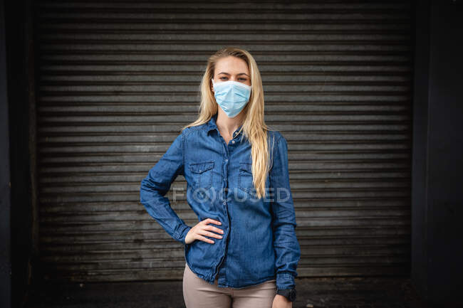 Ritratto di una donna caucasica dai lunghi capelli biondi, vestita con abiti casual e maschera contro l'inquinamento atmosferico e covid19 coronavirus, che guarda dritto in una macchina fotografica. — Foto stock