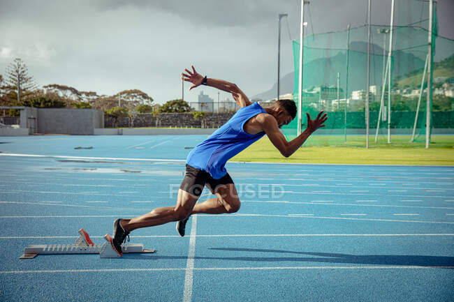 Side view of a mixed race male athlete practicing at a sports stadium, starting the race from starting blocks — Stock Photo