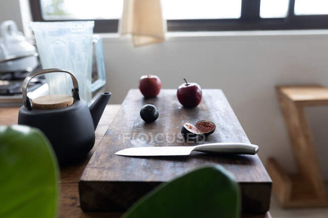 Primer plano de una tabla de cortar, cuchillo y frutas, manzana e higo en la mesa de la cocina. Preparación de alimentos en el hogar promoviendo un estilo de vida saludable. - foto de stock