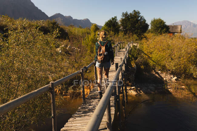 Visão traseira de uma mulher caucasiana se divertindo em uma viagem às montanhas, de pé em uma ponte, apreciando sua vista, em um dia ensolarado — Fotografia de Stock