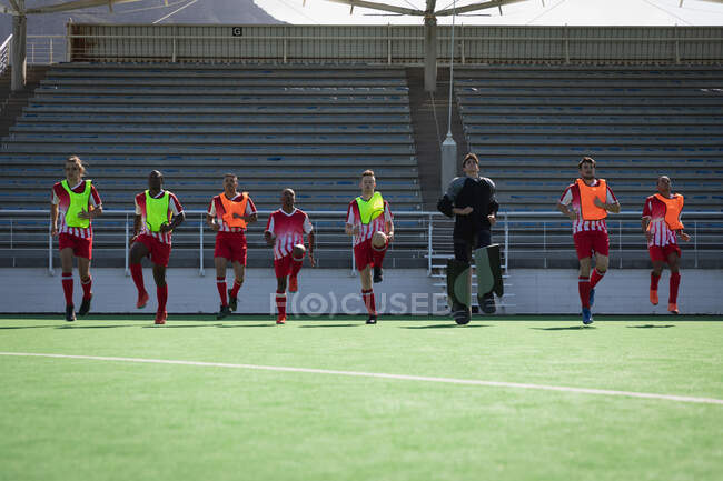 Front view of a multi-ethnic group of male field hockey players, training before a game, working out on a field hockey pitch, running on a sunny day — Stock Photo