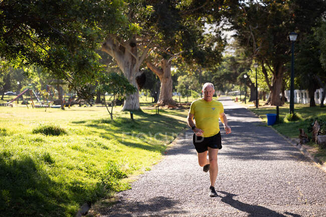 Vorderansicht eines athletischen älteren kaukasischen Mannes, der an einem sonnigen Tag in einem Park trainiert und auf einer Strecke läuft — Stockfoto