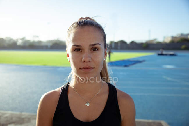 Ritratto di un'atleta caucasica sicura di sé con indosso un giubbotto nero che si esercita in uno stadio sportivo, guardando dritto alla macchina fotografica — Foto stock