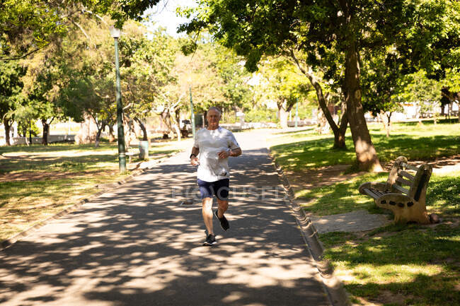 На перший погляд атлетичний старший кавказький чоловік працює в парку в сонячний день, біжить по доріжці. — стокове фото