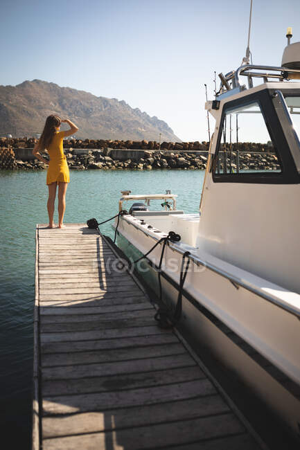 Una adolescente caucásica, disfrutando de su tiempo de vacaciones al sol en la costa, de pie en un embarcadero y mirando hacia otro lado - foto de stock