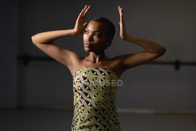 Front view close up of a mixed race female dancer wearing yellow dress, dancing in a studio with her hands up. — Stock Photo