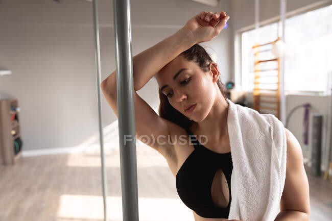 Front view of a fit attractive Caucasian woman enjoying pole dance training at a studio, taking a break, leaning on the pole with a towel on her shoulder — Stock Photo