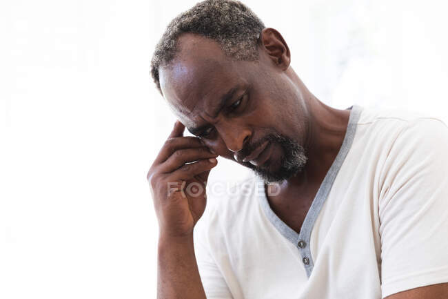 Крупным планом красивый пенсионер афроамериканец дома держит голову и смотрит вниз, брови нахмурены болью или глубокой мыслью, самоизоляция во время коронавируса covid19 пандемии — стоковое фото