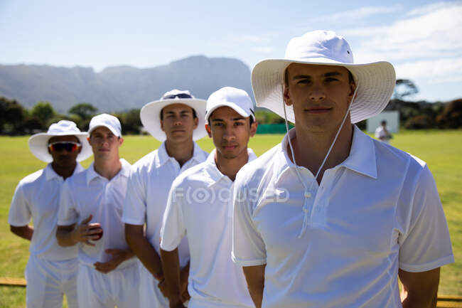 Front view close up of a teenage multi-ethnic male cricket team wearing whites, standing on the pitch together, looking straight to camera. — Stock Photo