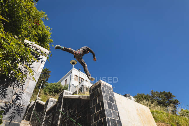 Vista lateral de baixo ângulo de um homem caucasiano praticando parkour pelo edifício em uma cidade em um dia ensolarado, pulando em corrimão escadas. — Fotografia de Stock