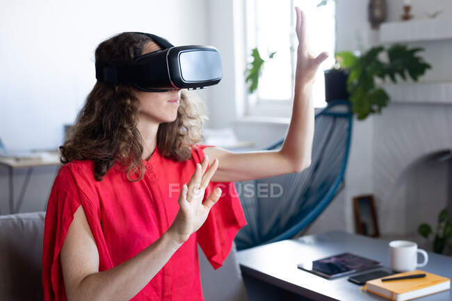 Caucasian woman spending time at home, wearing a pink dress, sitting on a sofa and using VR headset. Social distancing and self isolation in quarantine lockdown. — Stock Photo