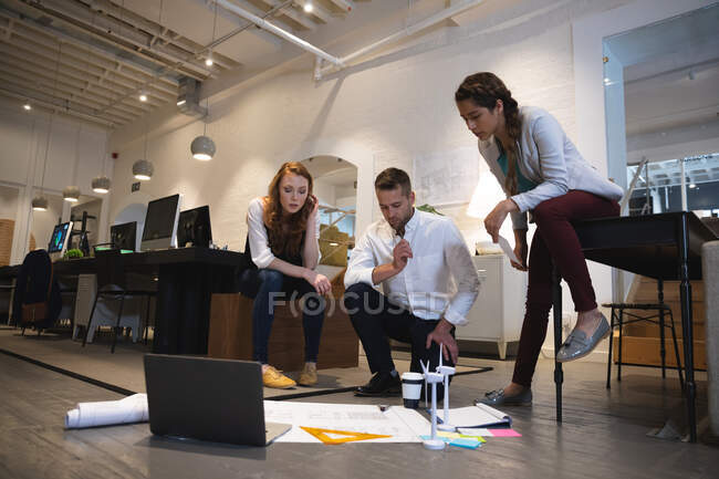 Caucasian female, male and a mixed race female business creatives working in a casual modern office, brainstorming together looking at plans — Stock Photo