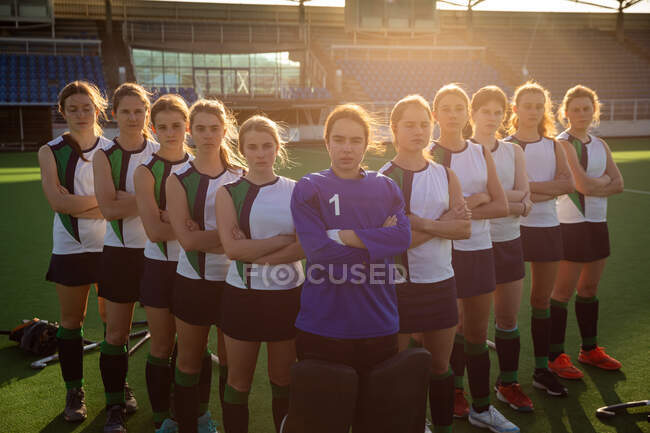 Front view of a group of confident female Caucasian field hockey players, preparing before a game, standing in a row, with arms crossed, looking at camera, on a sunny day — Stock Photo