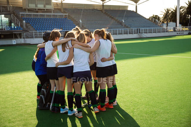 Side view of a group of female Caucasian field hockey players, preparing before a game, concentrating, motivating, huddling, on a sunny day — Stock Photo