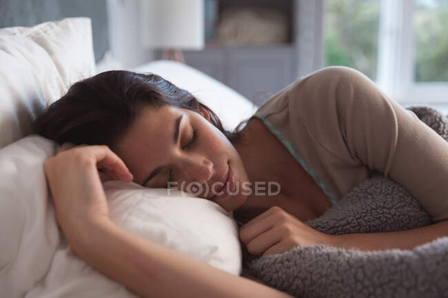 Femme métisse passant du temps à la maison auto-isolante et distanciation sociale en quarantaine verrouillée pendant l'épidémie de coronavirus covid 19, couchée au lit dormant. — Photo de stock