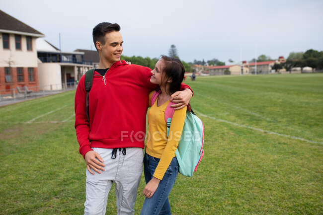 Vista frontal de uma mulher caucasiana e alunos do ensino médio masculinos saindo e abraçando uns aos outros, em pé em seus terrenos escolares — Fotografia de Stock