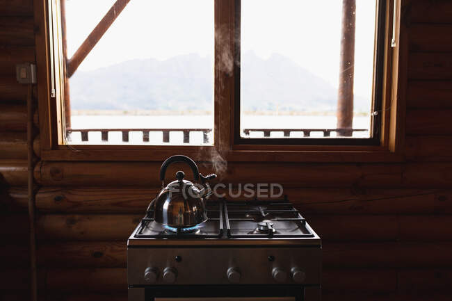 Detalhe de perto de uma chaleira em pé sobre um aquecedor em uma cabine de madeira nas montanhas, perto do lago, visto da janela — Fotografia de Stock