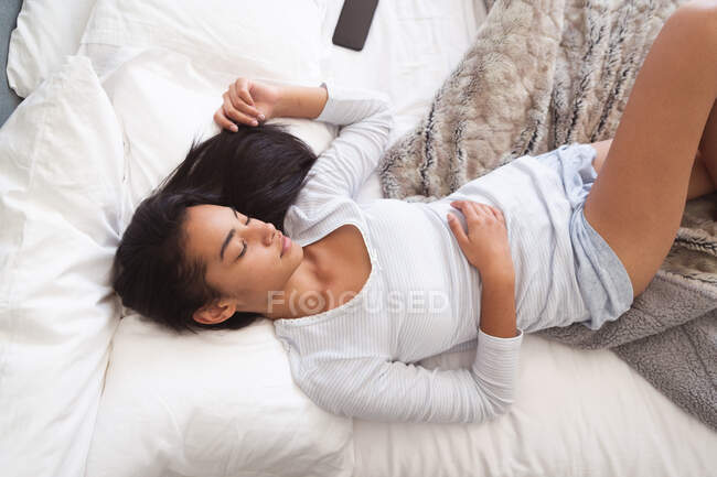 Mixed race woman spending time at home, lying on bed and sleeping in bedroom. Self isolating and social distancing in quarantine lockdown during coronavirus covid 19 epidemic. — Stock Photo