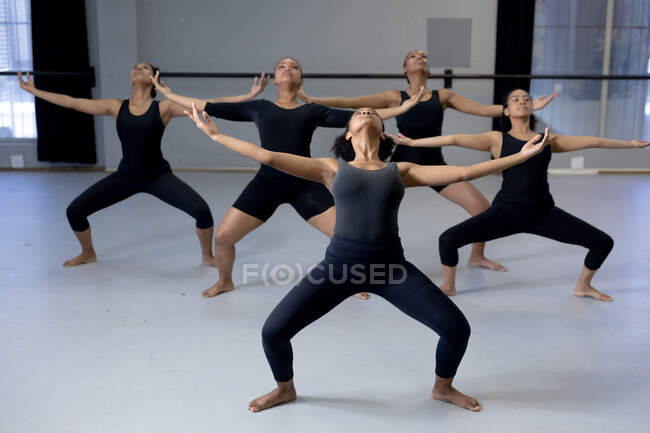 Vista frontale di un gruppo multietnico di ballerine moderne in forma che indossano abiti neri praticando una routine di danza durante una lezione di danza in uno studio luminoso, allargando le braccia. — Foto stock