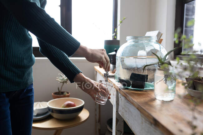 Mid section of woman spending time at home, pouring water. Lifestyle at home isolating, social distancing in quarantine lockdown during coronavirus covid 19 pandemic. — Stock Photo