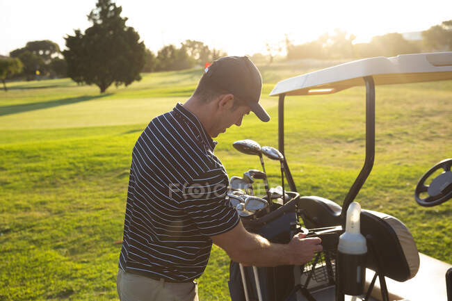 Seitenansicht eines kaukasischen Mannes auf einem Golfplatz, der seine Golftasche in einen Golfwagen legt, mit hellem Sonnenlicht — Stockfoto